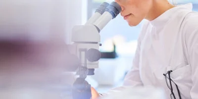 白衣姿で顕微鏡をのぞく研究者