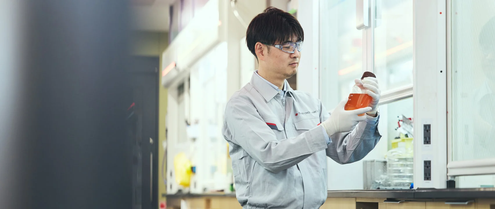 研究室で薬液入りフラスコを持つK. M.