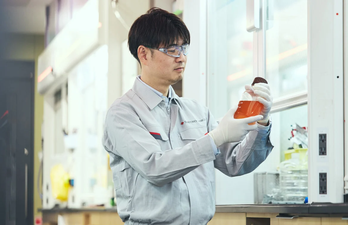 研究室で薬液入りフラスコを持つK. M.