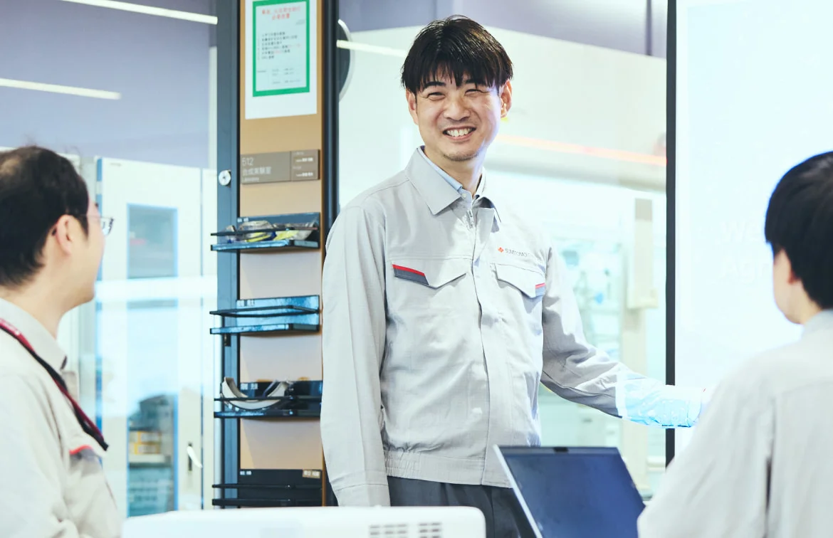 研究室で同僚に説明するK. M.