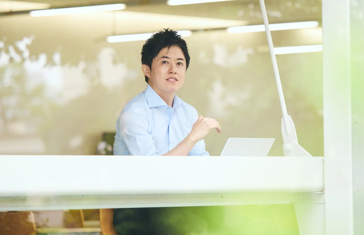 窓越しにノートPCに向かうF. H.