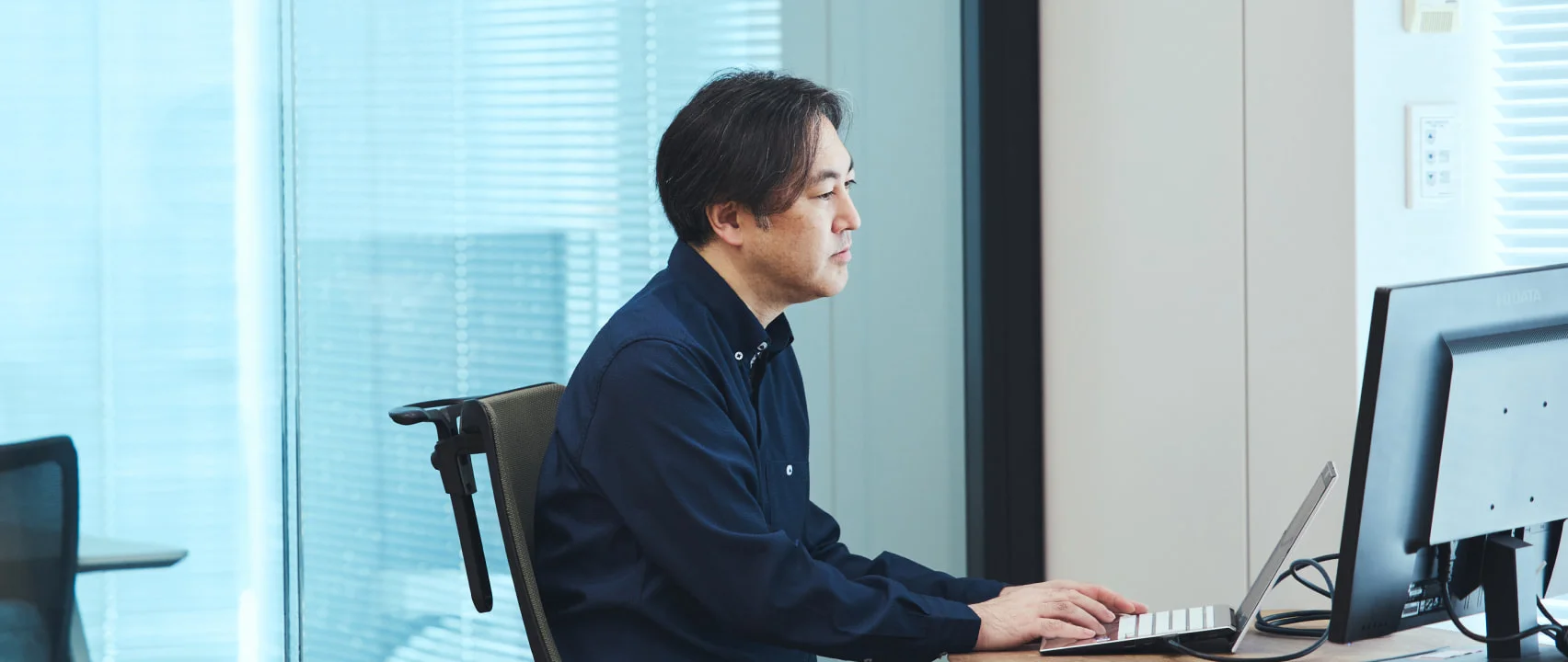 デスクでノートPCとモニターに向かうS. T.
