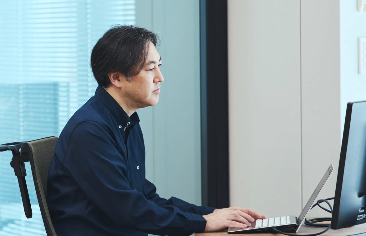 デスクでノートPCとモニターに向かうS. T.