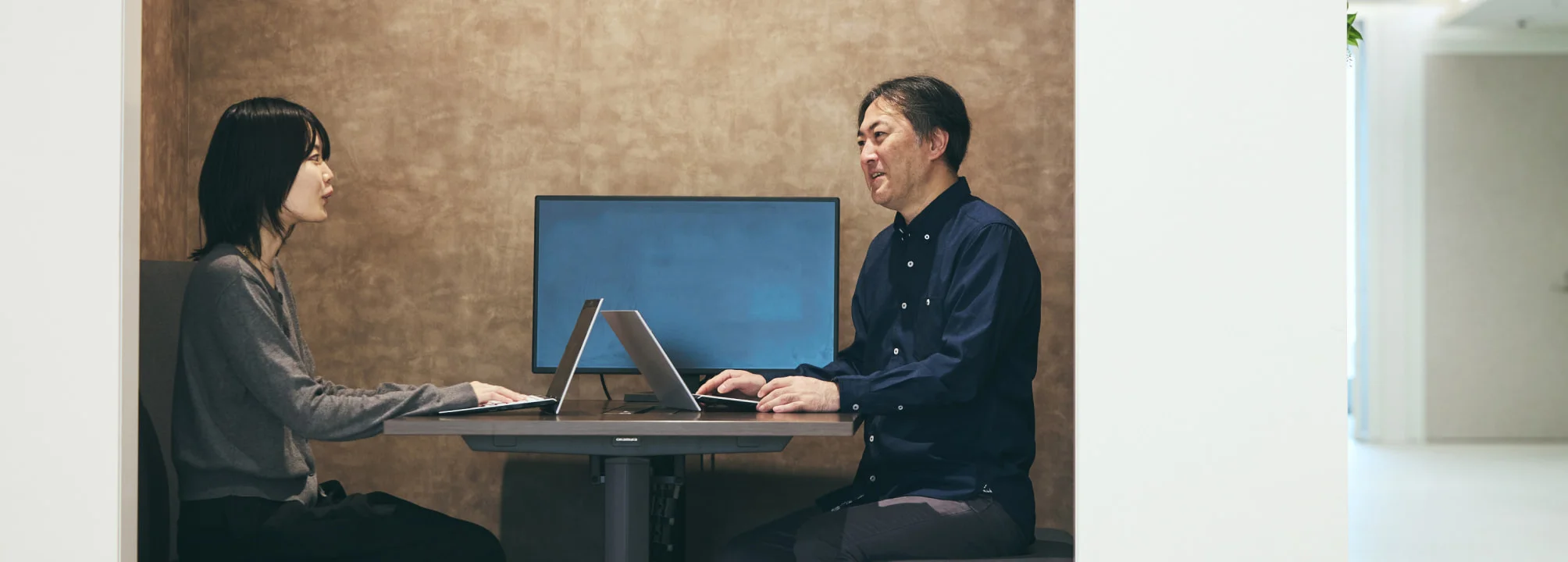 同僚とモニターを挟んで話すS. T.